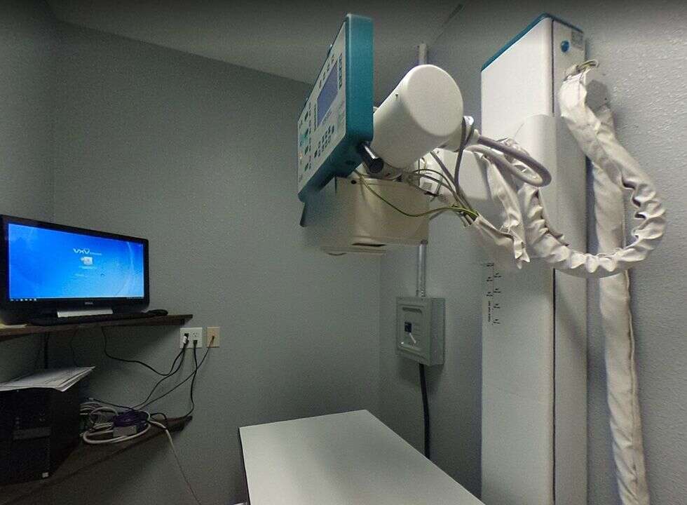 A medical examination room featuring an X-ray machine and a computer on a wall-mounted shelf.