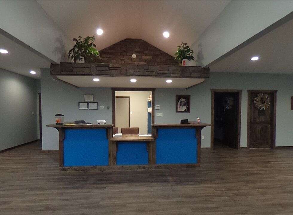 A modern reception desk with a blue front, surrounded by potted plants and wall decor in a well-lit room.