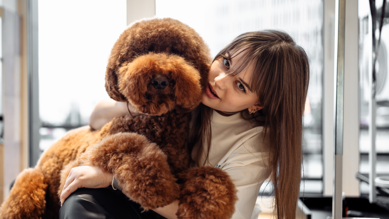 A girl leans in closely with a fluffy brown dog, both smiling and enjoying each other's company.